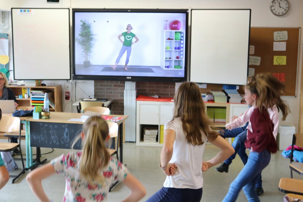 Kinder tanzen vor einem Bildschirm in einem Klassenzimmer.