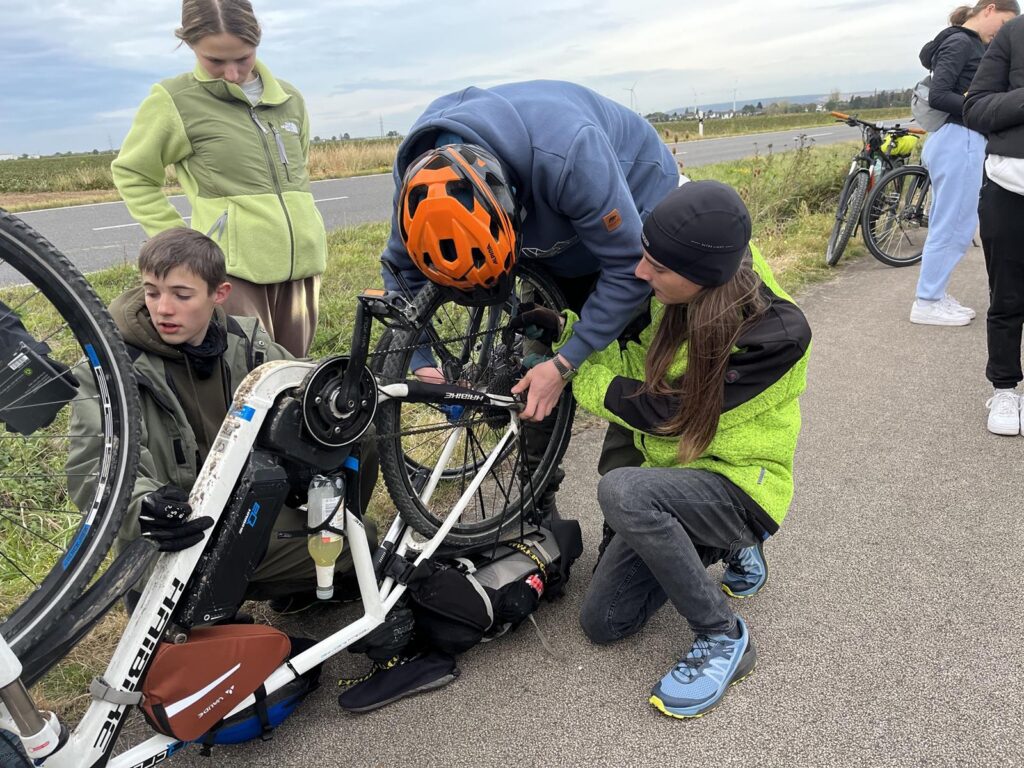 Gruppe von Jugendlichen repariert ein Fahrrad am Straßenrand.