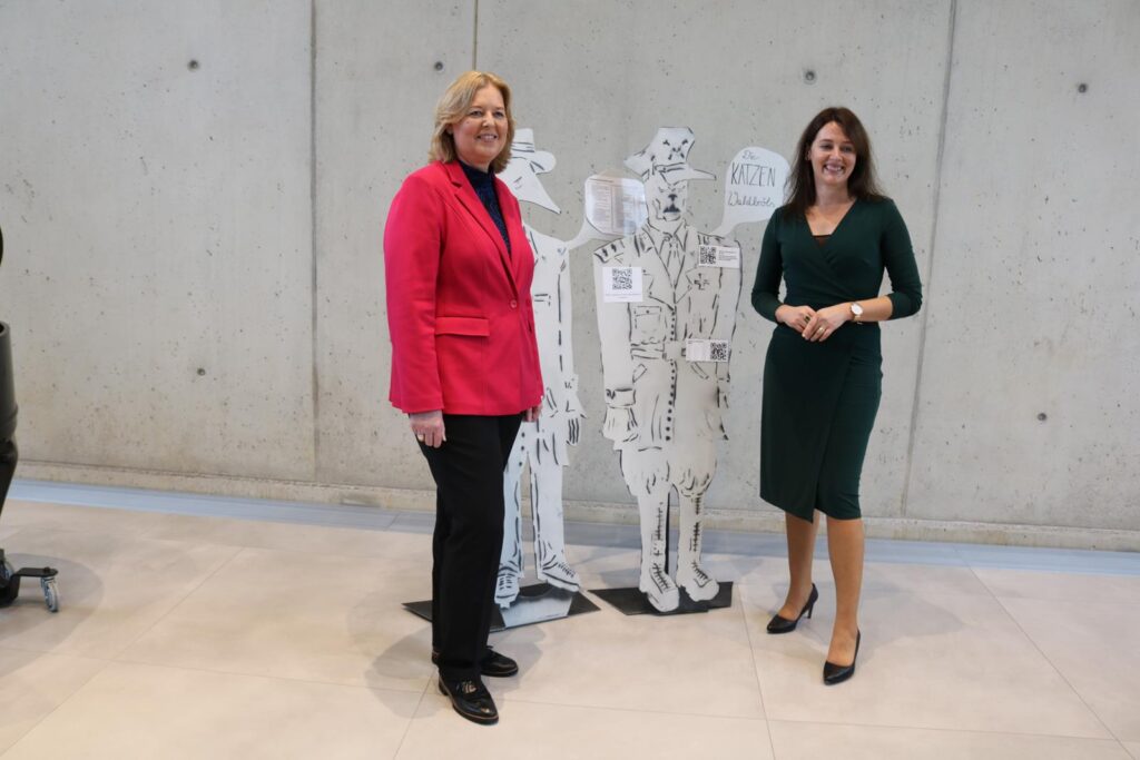 Zwei Frauen stehen neben transparenten Figuren in einem modernen Raum.