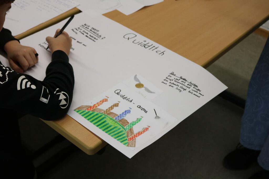 Ein Schüler schreibt an einem Plakat mit bunten Zeichnungen und Text.