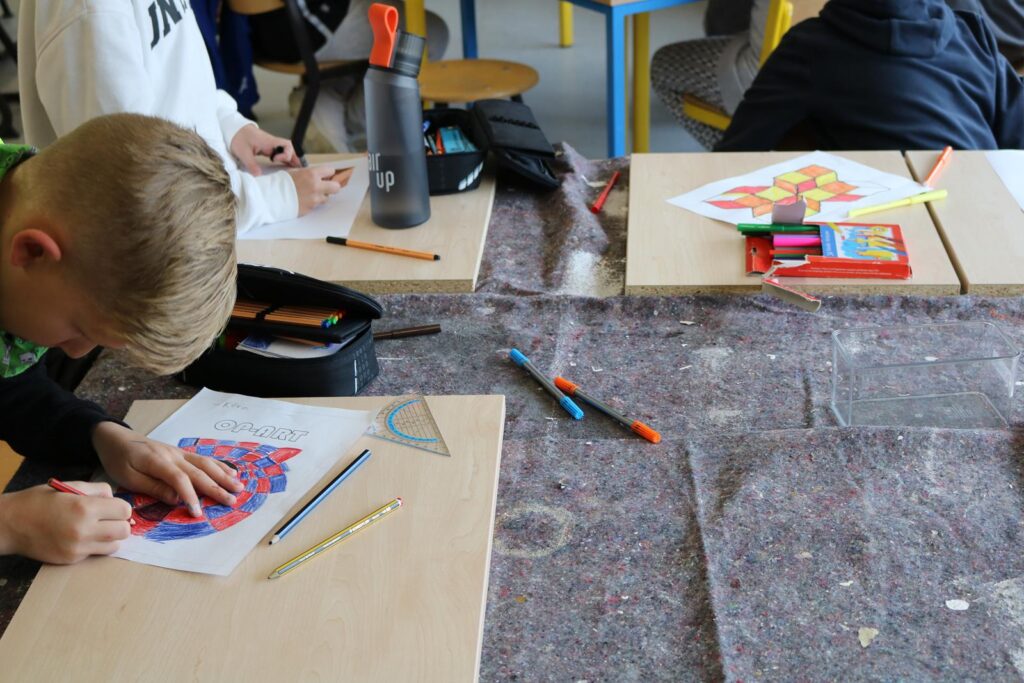 Kinder malen an Tischen mit Stiften und Malutensilien.