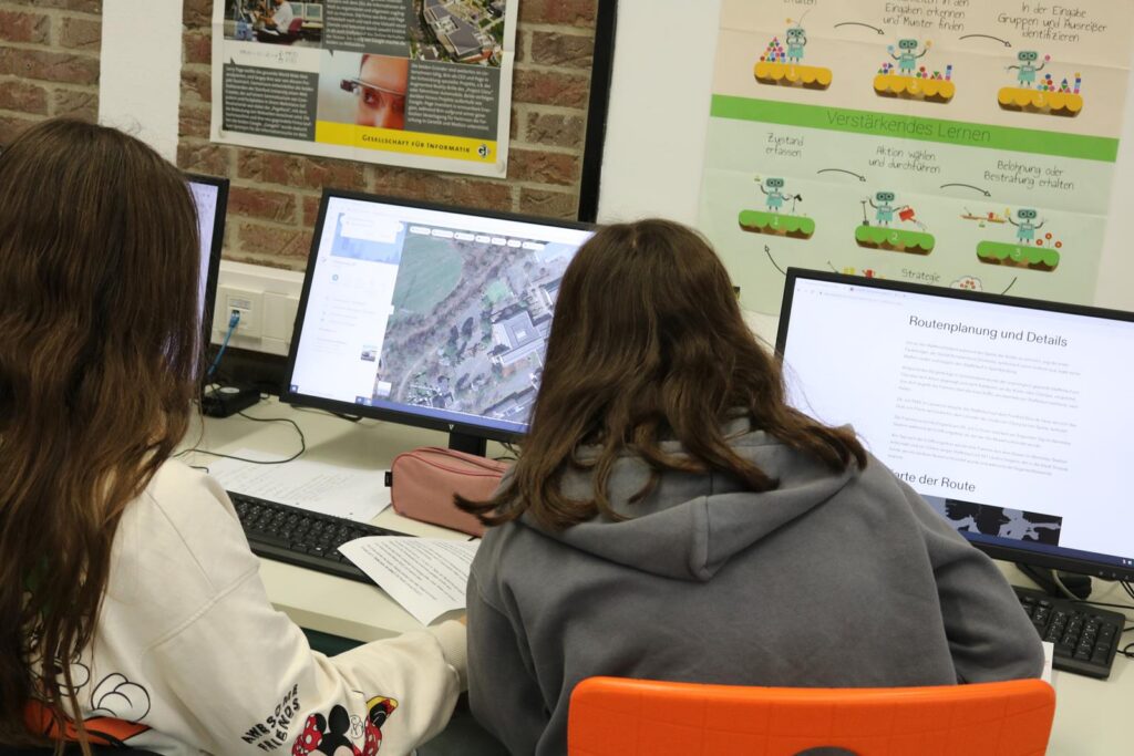 Zwei Schülerinnen arbeiten an Computersystemen in einem Klassenraum.