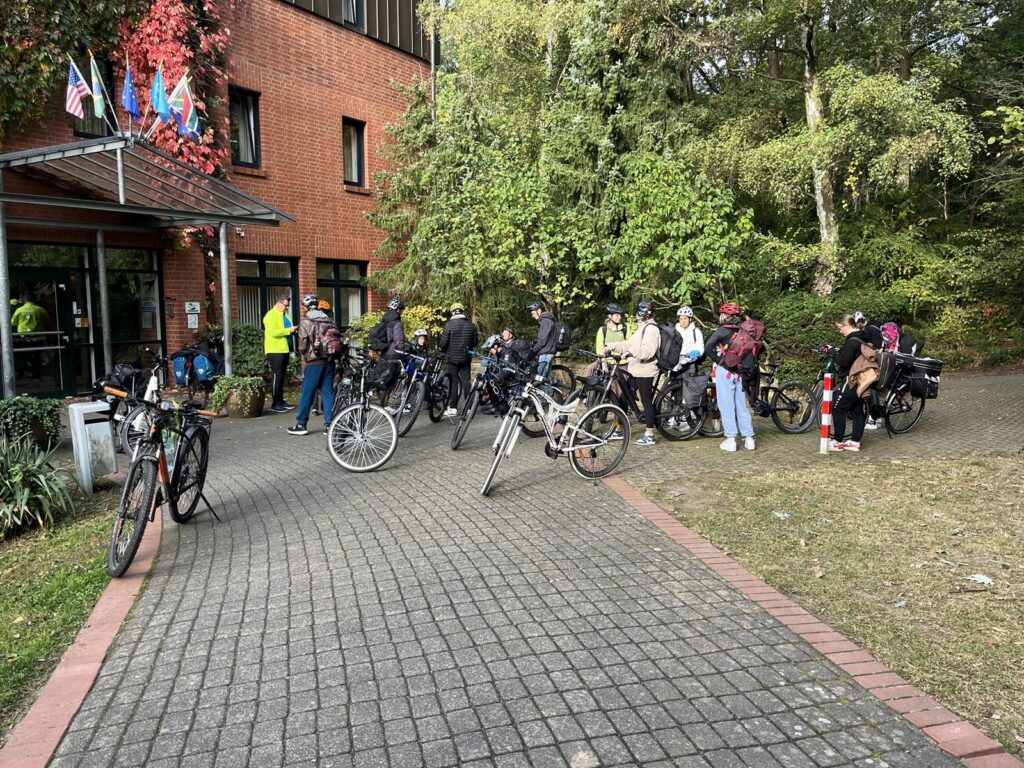 Gruppierung von Fahrradfahrern vor einem Gebäude, umgeben von Bäumen.