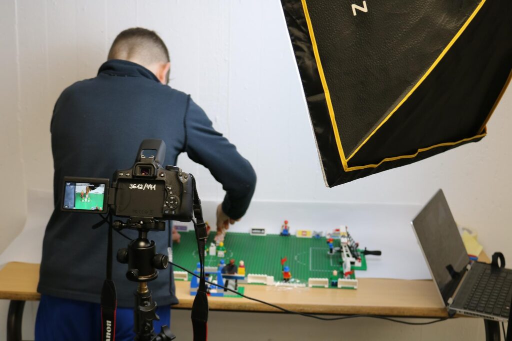 Ein Junge baut eine LEGO-Fußballspielszene vor einer Kamera auf.
