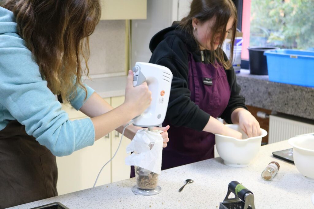 Zwei Personen backen in einer Küche mit einem Handmixer und einer Schüssel.