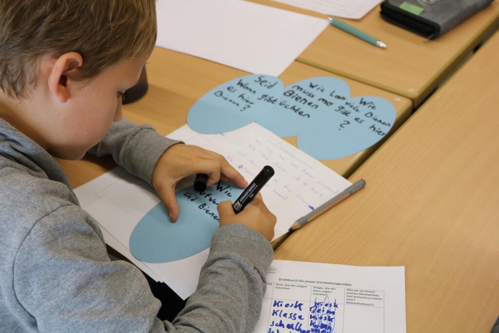 Ein Junge schreibt mit einem Marker auf Papier an einem Tisch.