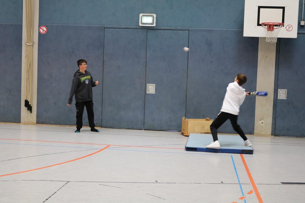 Schüler wirft einen Ball in der Sporthalle, während ein anderer zusieht.