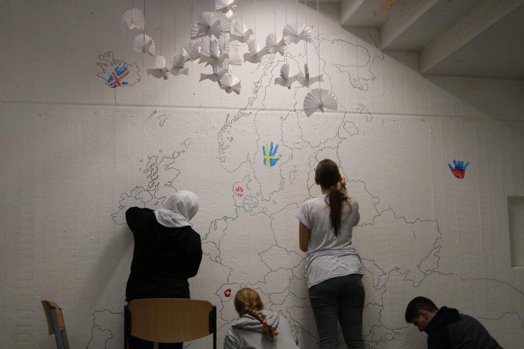 Drei Personen gestalten eine große Europakarte an einer Wand.