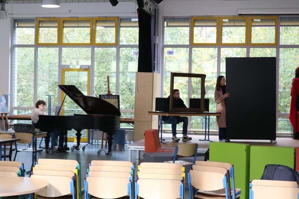 Schüler am Klavier und zwei Personen an Stellwänden in einem Klassenraum.