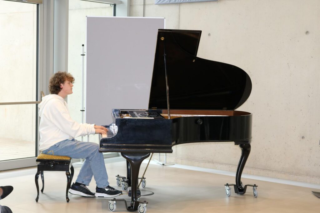 Ein junger Mann spielt Klavier in einem hellen Raum.
