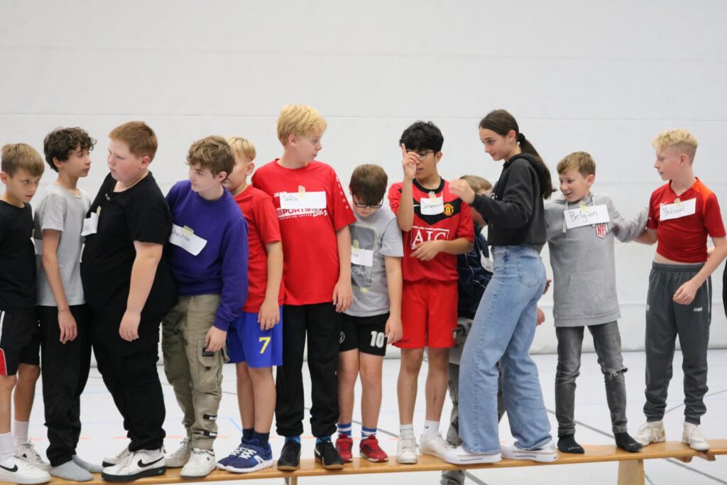 Gruppen von Schülern stehen auf einer Bank in Sportkleidung.