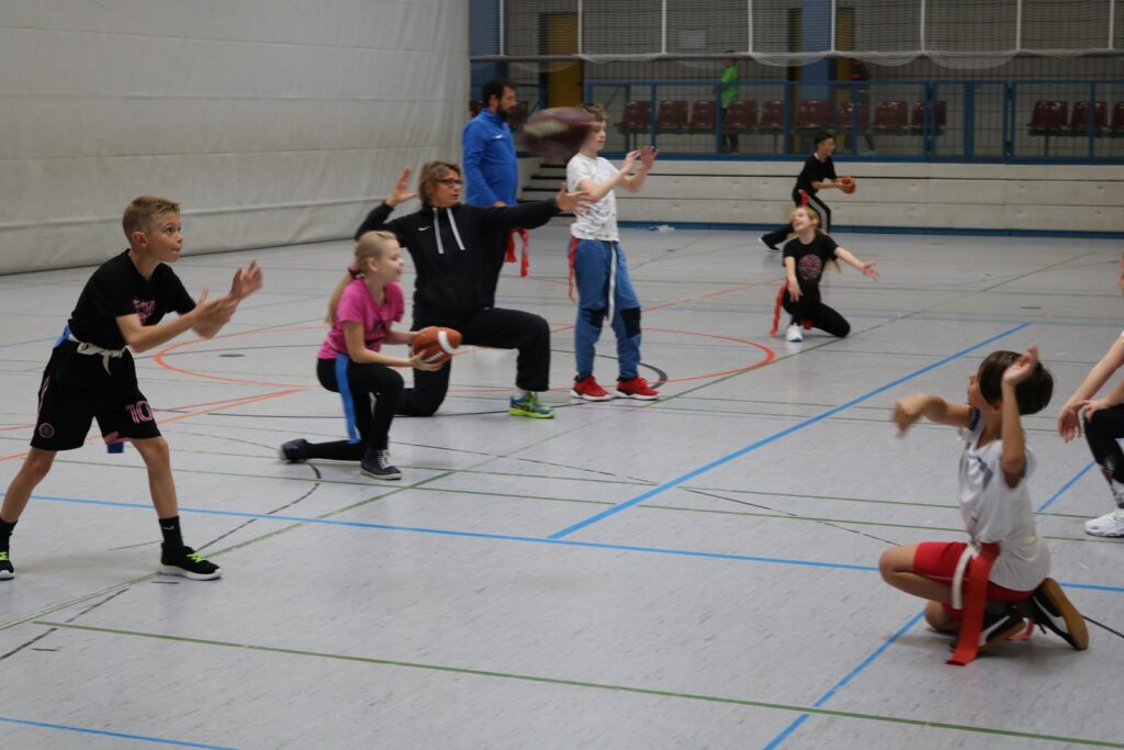 Kinder und Erwachsene im Sportunterricht bei verschiedenen Übungen in einer Halle.