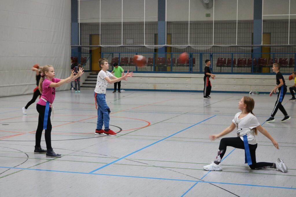 Schüler spielen in einer Sporthalle mit Bällen.