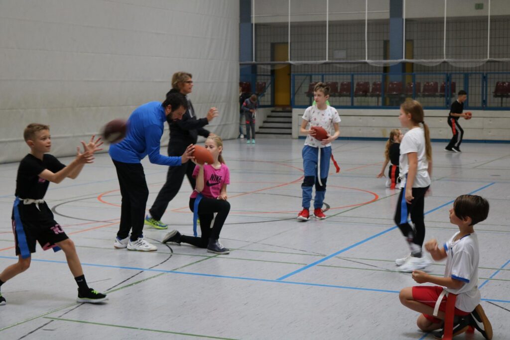 Kinder und Trainer spielen Basketball in einer Sporthalle.