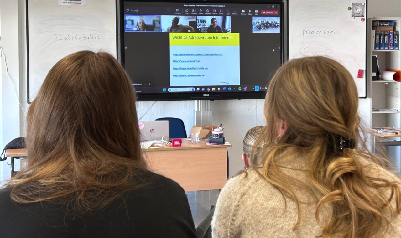 Zwei Schülerinnen sitzen vor einem Bildschirm mit Videokonferenz.