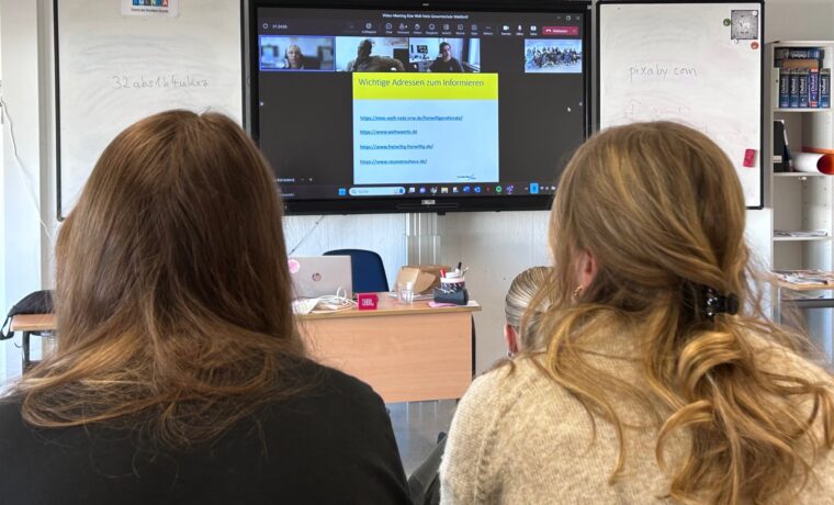 Zwei Schülerinnen sitzen vor einem Bildschirm mit Videokonferenz.