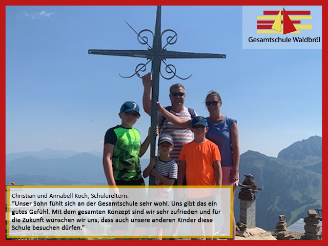 Familie Koch steht mit einem Kreuz auf einem Berggipfel. Hintergrund: Berge und Himmel.