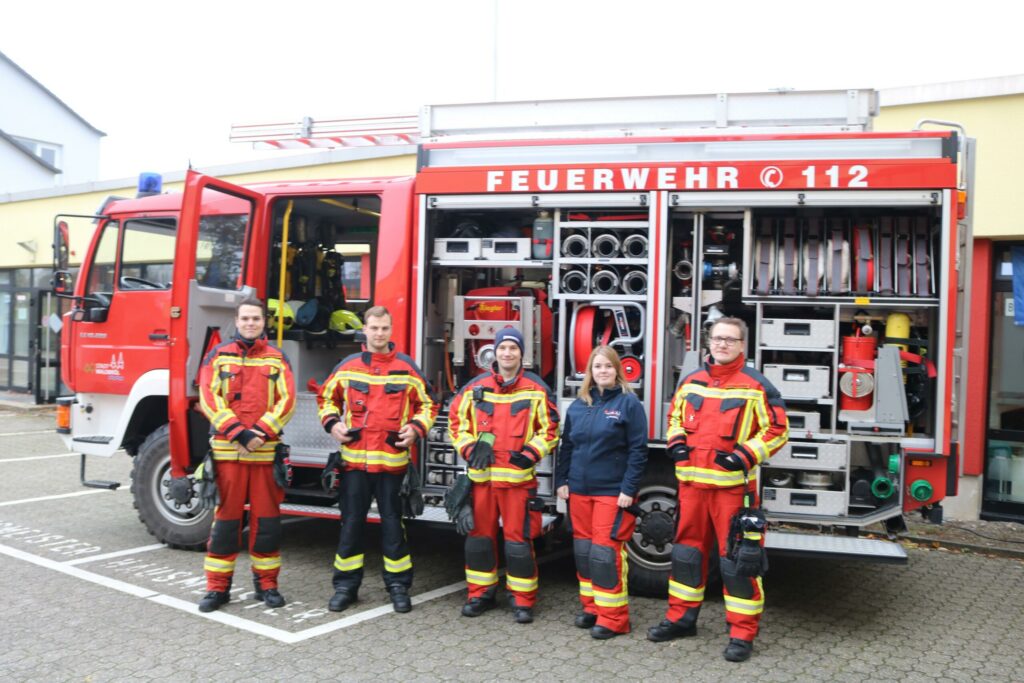 Feuerwehrleute stehen vor einem Feuerwehrauto mit Ausrüstung.