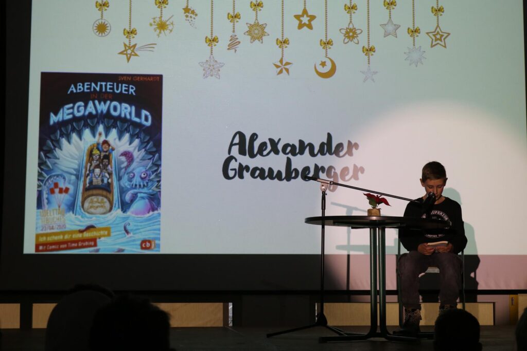 Junge sitzt an einem Tisch, liest vor einer Präsentation über "MegaWorld".