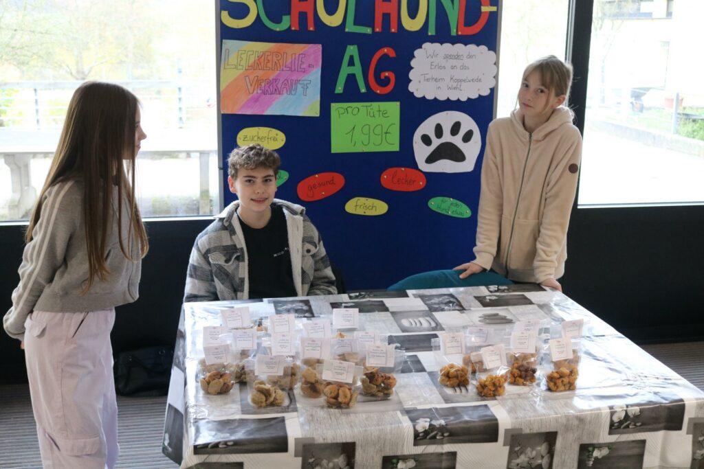 Schülerinnen und Schüler stehen an einem Tisch mit Plakaten und Leckereien.