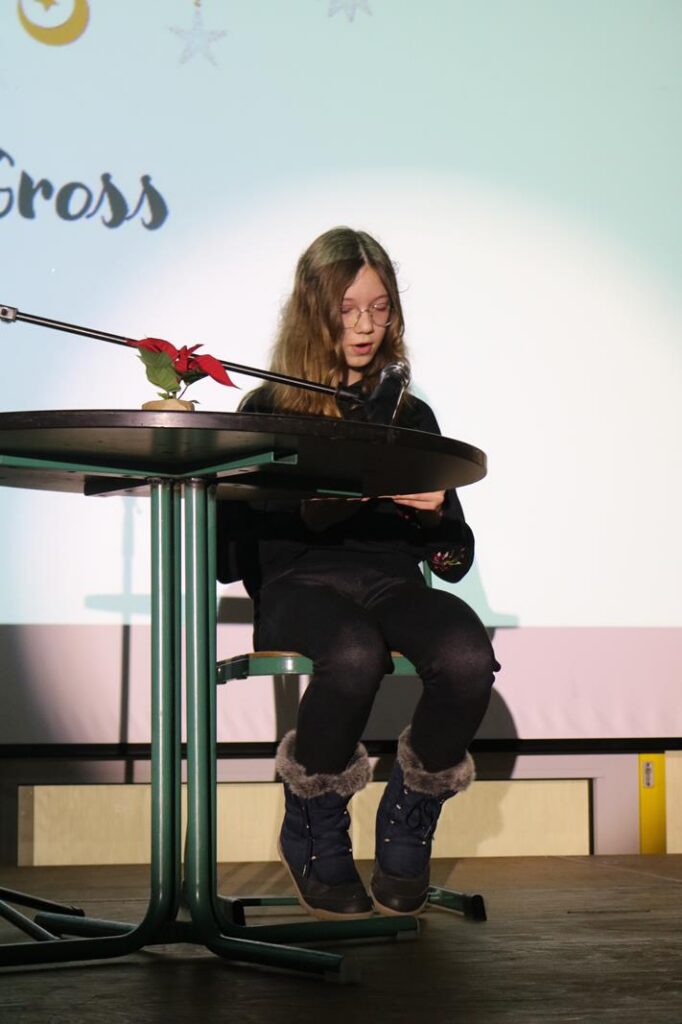 Ein Mädchen sitzt an einem Tisch und liest von einem Blatt.