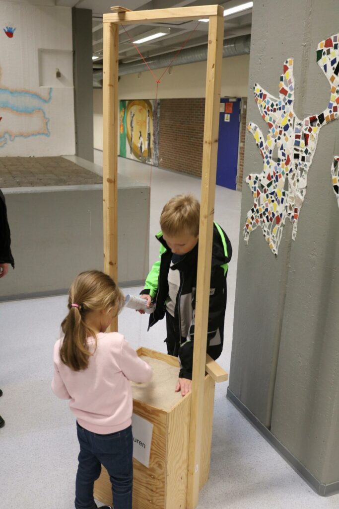 Kinder stecken Zettel in eine Wahlurne in einem Schulflur.