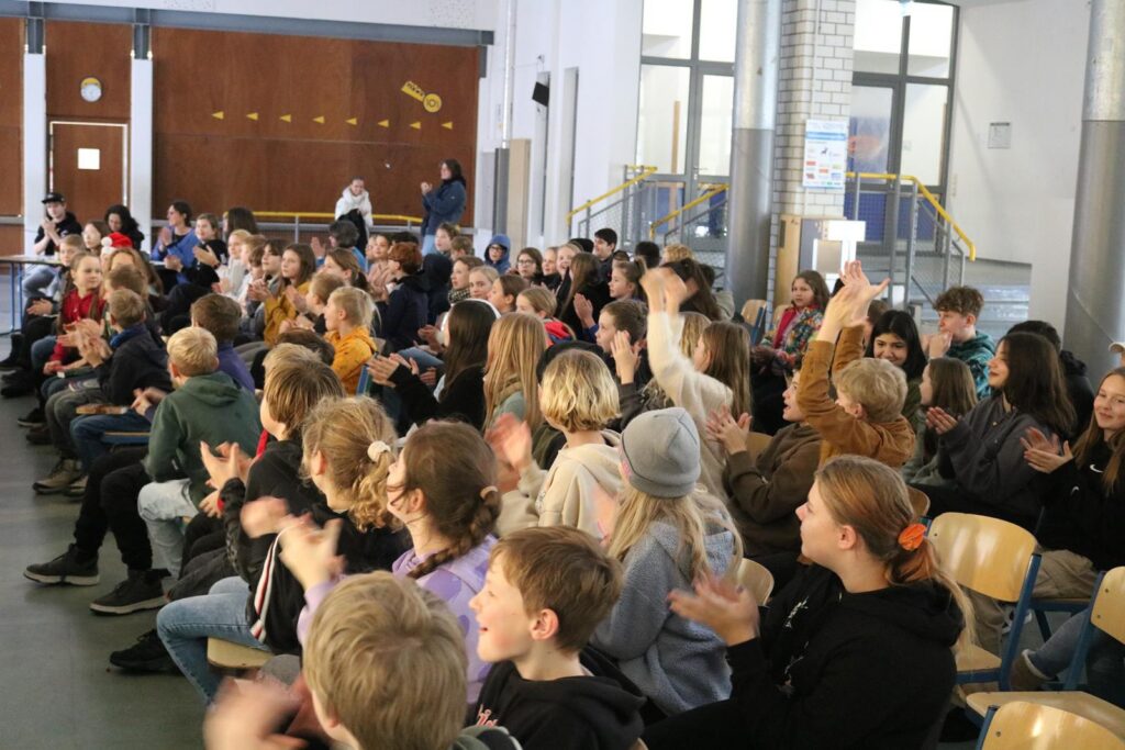 Schüler sitzen in einem Raum und applaudieren begeistert.