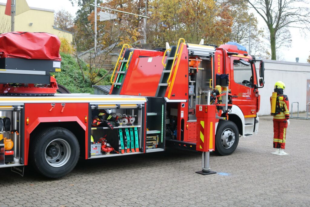 Feuerwehrauto mit Ausrüstung, Feuerwehrmann steht daneben. Herbstliche Umgebung.