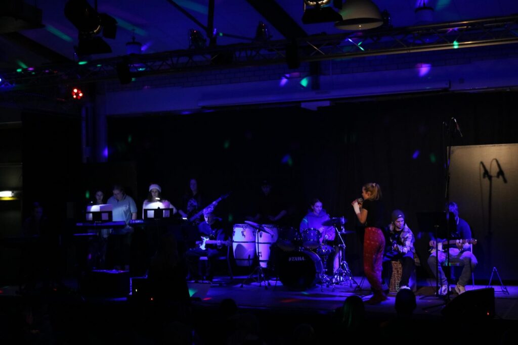 Band spielt auf einer Bühne mit bunten Lichtern und einem Sänger.