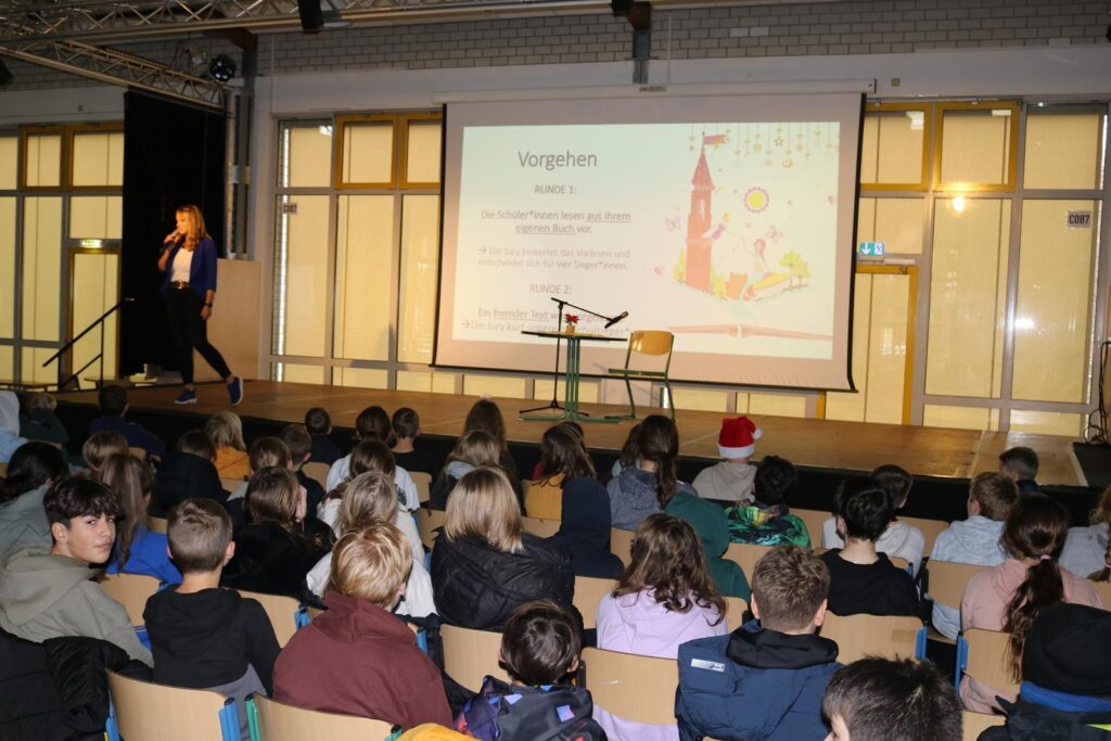 Schüler sitzen im Publikum, während eine Person auf der Bühne spricht.