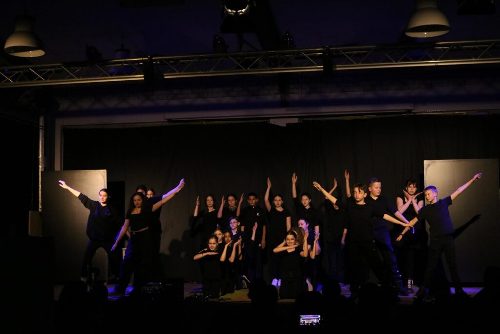 Schüler in schwarzen Kostümen stehen auf der Bühne und führen eine Choreographie auf.