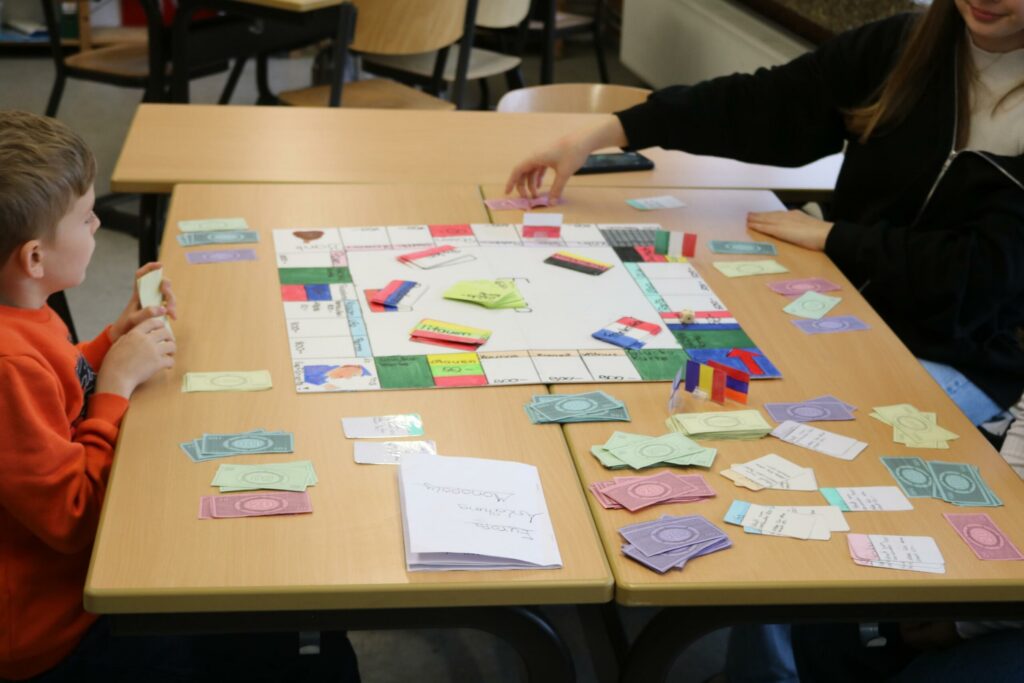 Kinder spielen ein Brettspiel an einem Tisch in einem Klassenraum.