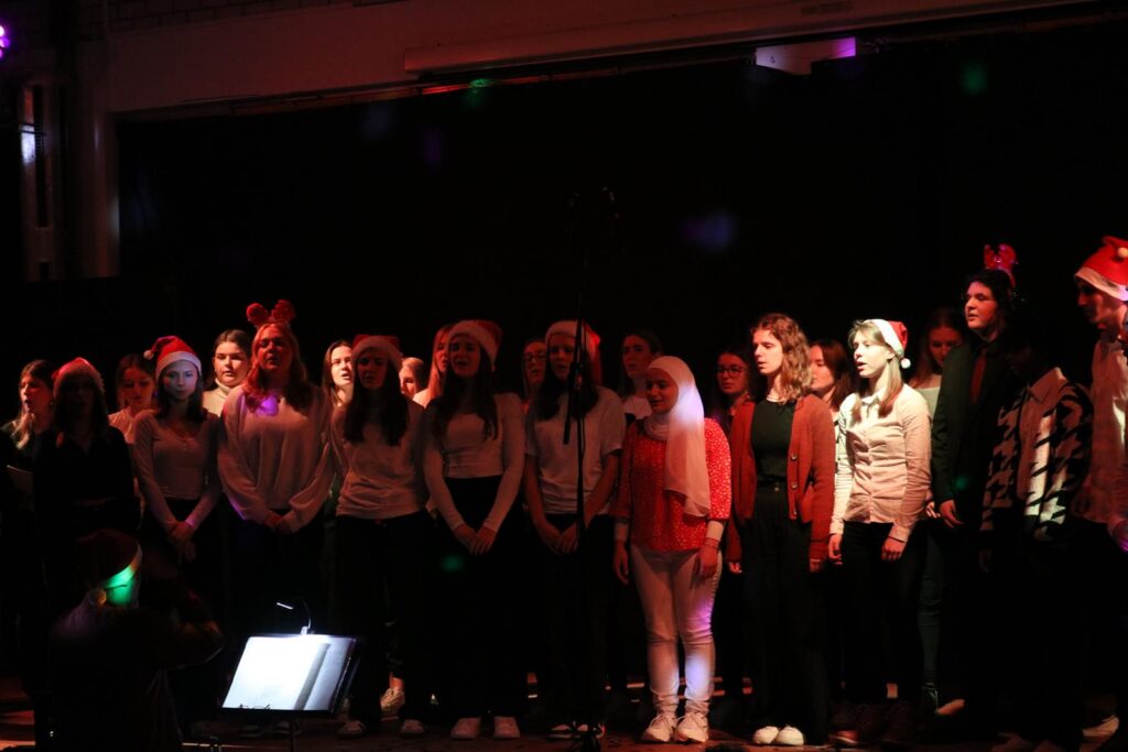 Schülerinnen und Schüler singen auf einer Bühne mit buntem Licht.