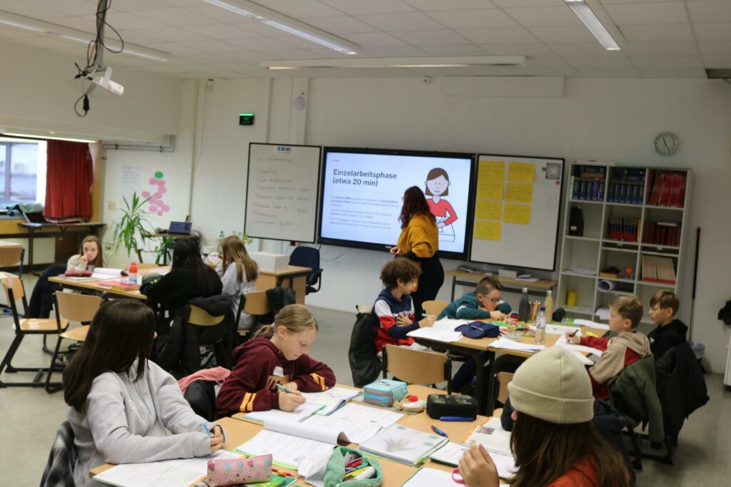 Schulklasse mit Schülern und Lehrerin an einem interaktiven Bildschirm.