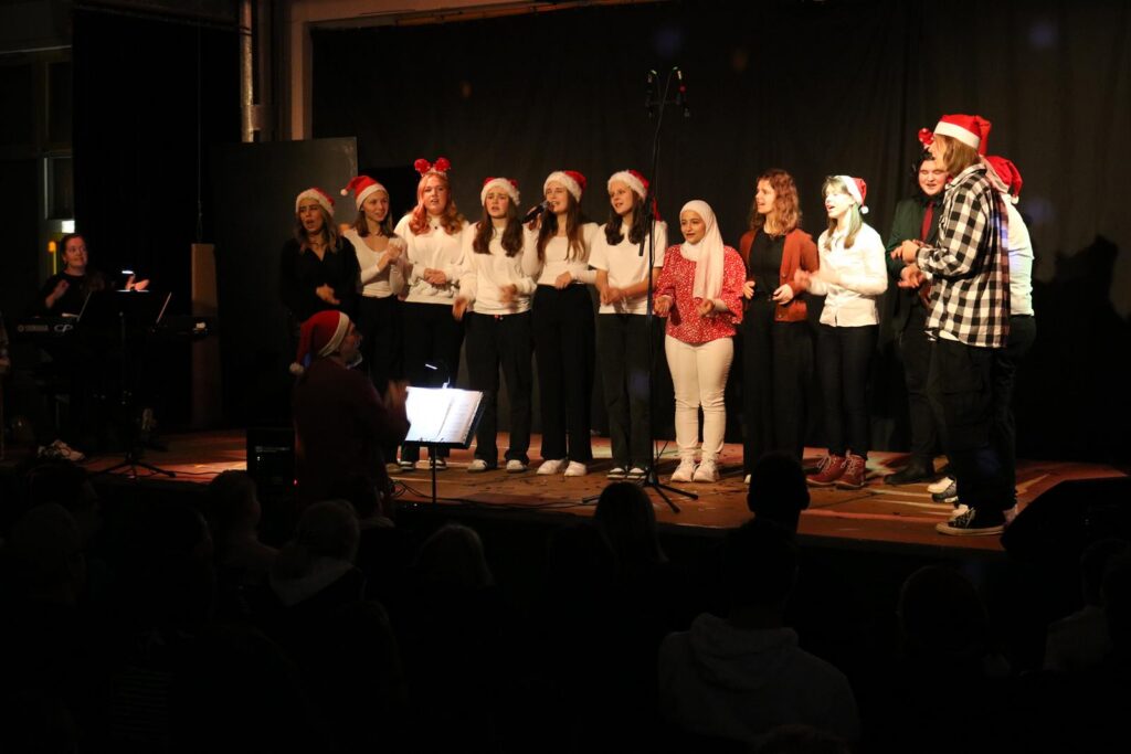 Schülerinnen und Schüler singen im Weihnachtskostüm auf einer Bühne.