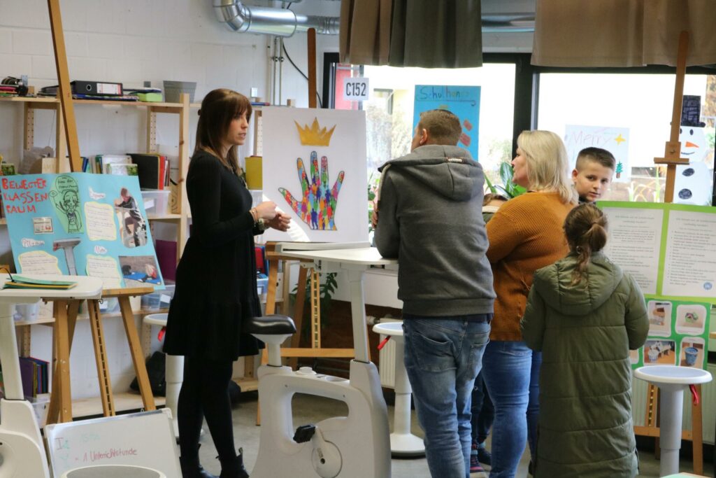 Besucher stehen vor Kunstwerken in einem Klassenzimmer.