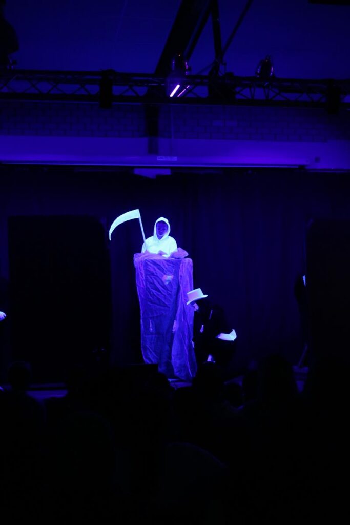 Schauspieler in schwarzer Umgebung mit leuchtender Grim-Reaper-Verkleidung.