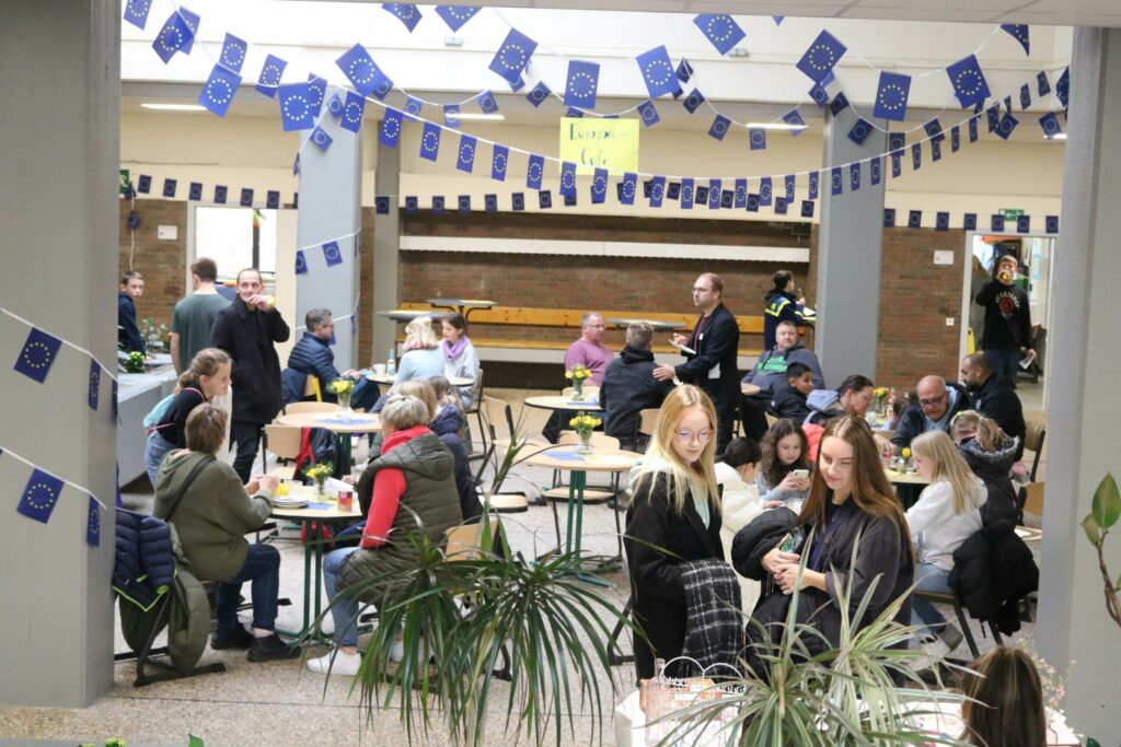 Menschen sitzen an Tischen in einer geschmückten Halle und unterhalten sich.