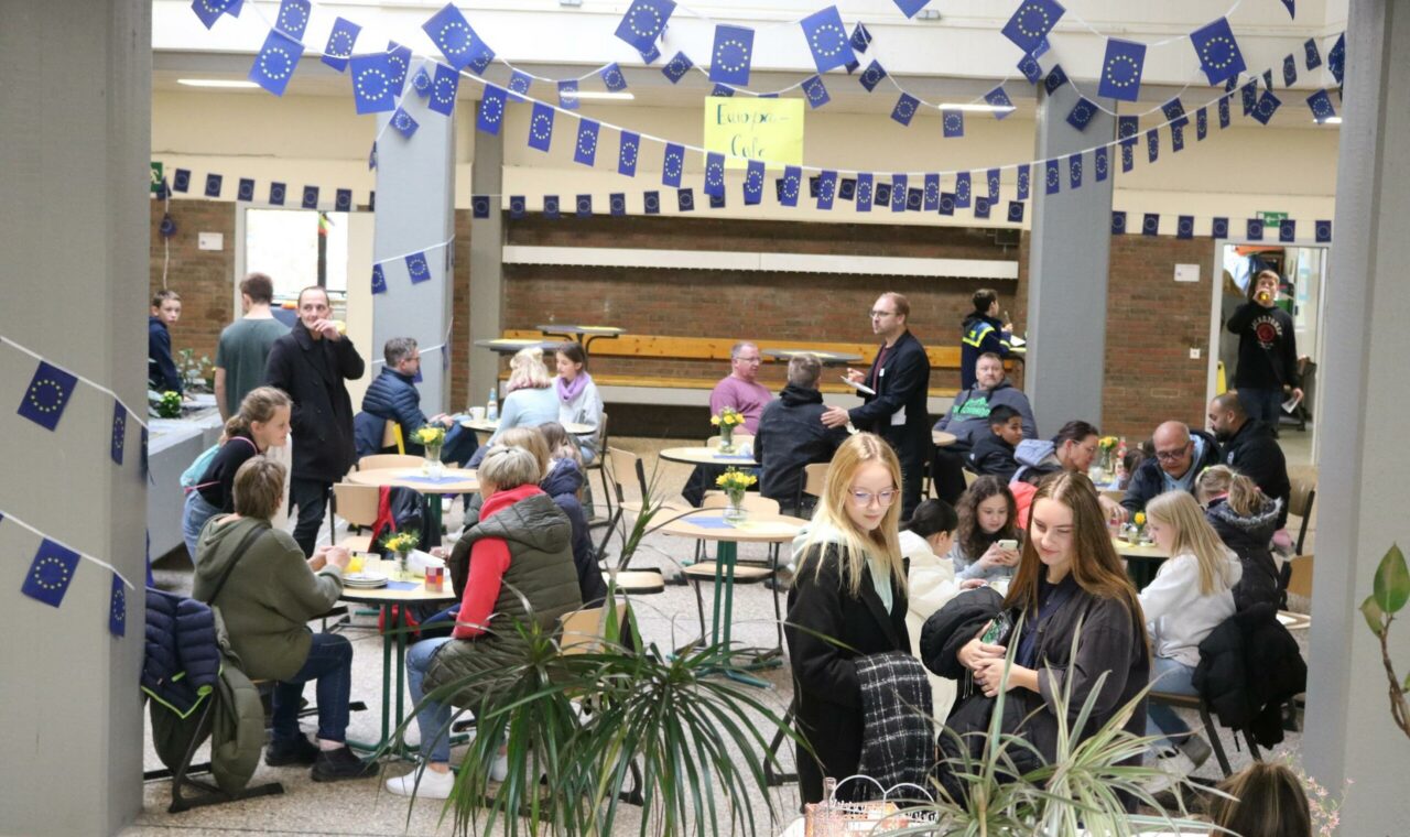 Menschen sitzen an Tischen in einer geschmückten Halle und unterhalten sich.