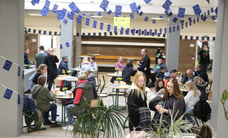 Menschen sitzen an Tischen in einer geschmückten Halle und unterhalten sich.