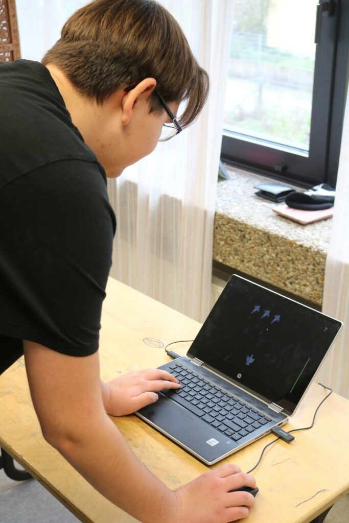 Schüler arbeitet an einem Laptop an einem Tisch neben einem Fenster.