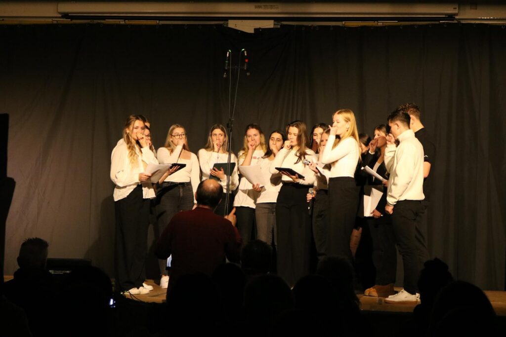 Schüler singen auf einer Bühne vor einem dunklen Vorhang.
