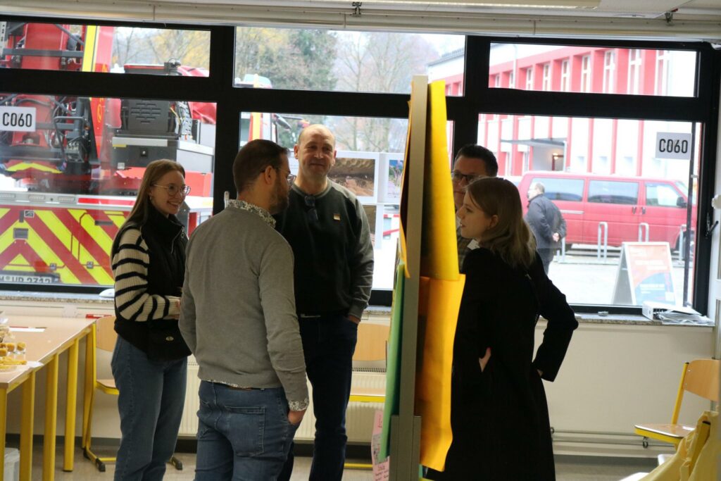 Gruppe von fünf Personen in einem modernen Raum, im Hintergrund ein Feuerwehrauto.