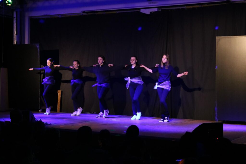 Fünf Tänzerinnen führen eine Choreografie auf einer Bühne vor.