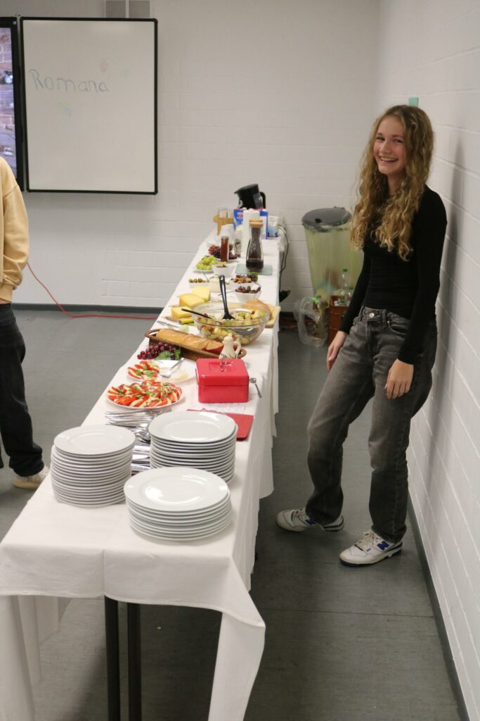 Junge Frau steht neben einem Tisch mit Essen und Getränken.