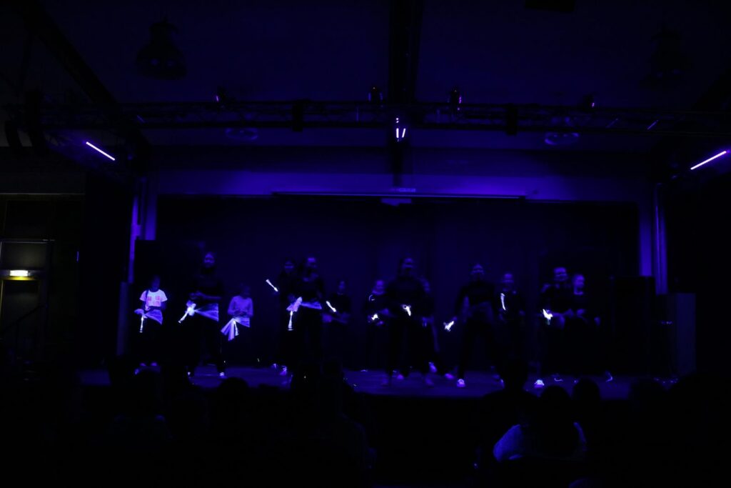 Dunkle Bühne mit tanzenden Personen, beleuchtet von blauen Lichtakzenten.