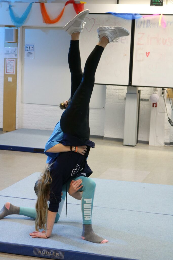 Zwei Schülerinnen üben einen Handstand auf einer Turnmatte.