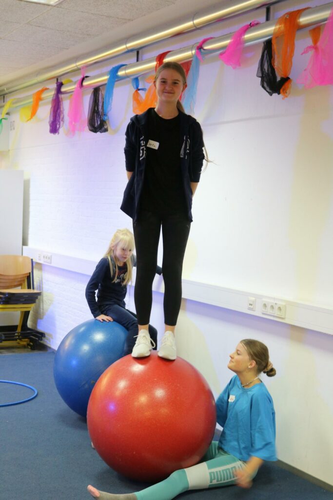 Drei Kinder üben auf großen Bällen in einem Raum mit bunten Dekorationen.
