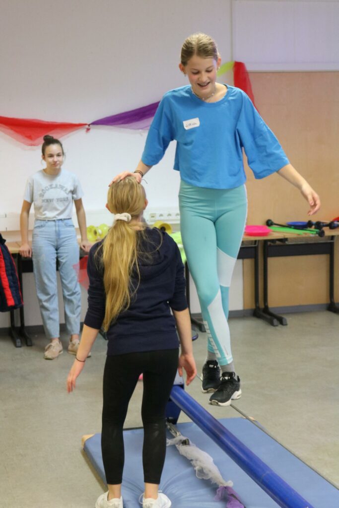Zwei Mädchen üben auf einem Schwebebalken in einer Turnhalle.
