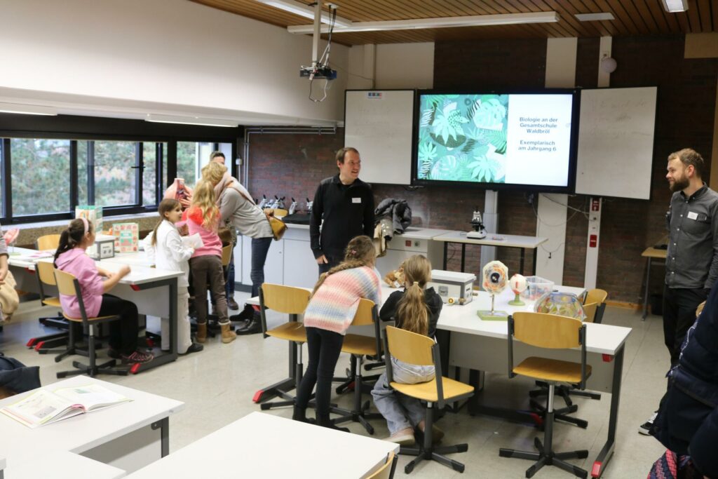 Ein Klassenraum mit Kindern, Lehrern und Präsentationstechnik.